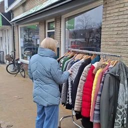 Klant bekijkt tweedehands kleding aan een rek buiten de winkel