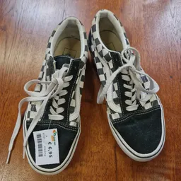 Paar zwart-witte geruite Vans-sneakers met veters op houten vloer
