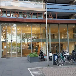 Gevelvoorzijde van kringloopwinkel met grote glazen pui, fietsenstalling en ingangen aan straat