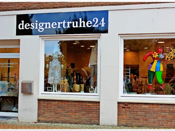 Winkelpui van designertruhe24 met grote ramen, zwart naambordje en etalage met decoratieve items