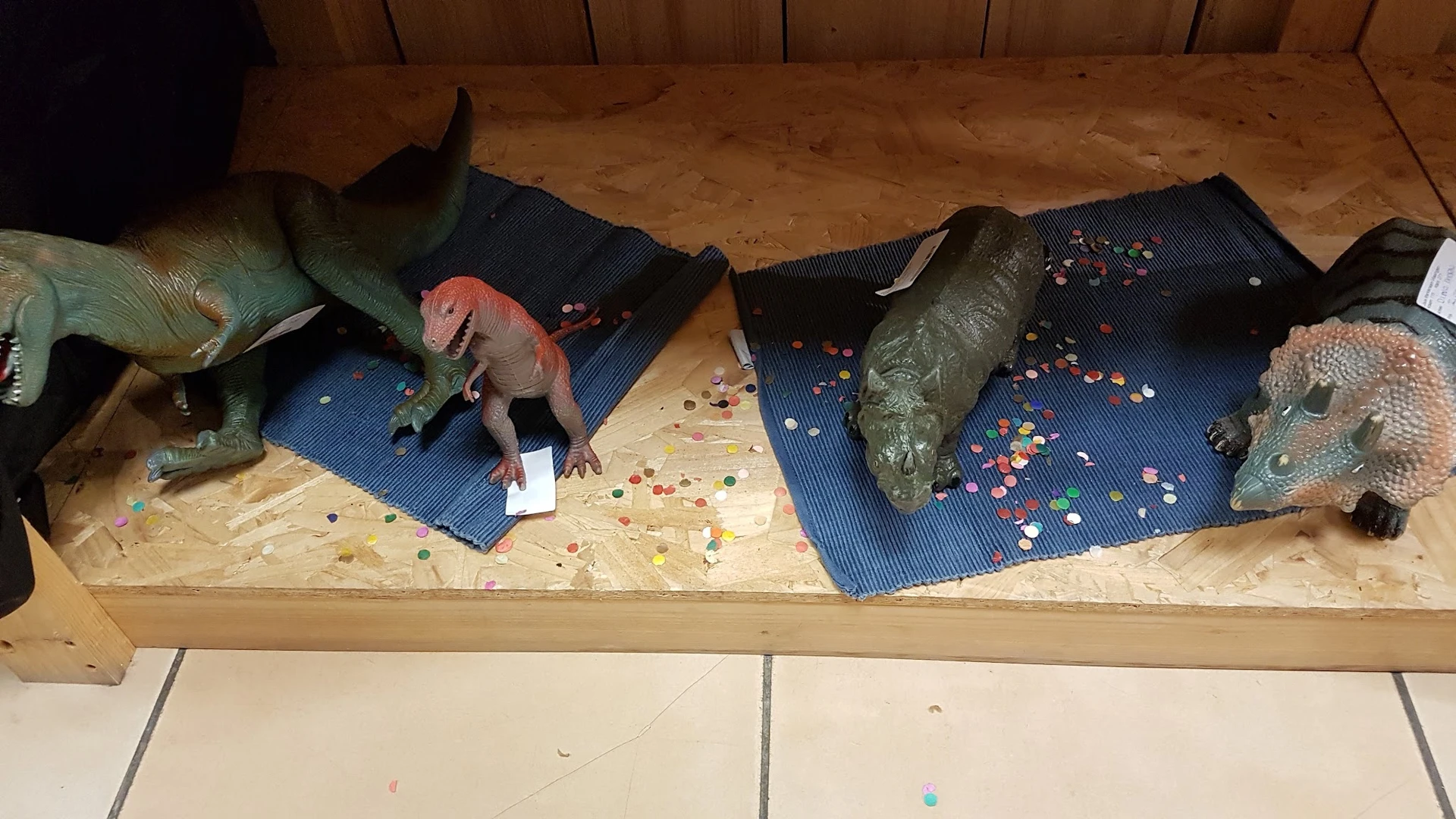 Drie reptielmodellen op blauwe ondergronden met gekleurde steentjes, uitgestald op een houten plank