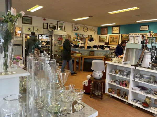 Winkelvloer van kringloopwinkel met glazen serviesgoed op de voorgrond, stellingen met spullen, afdelingen op de achtergrond 