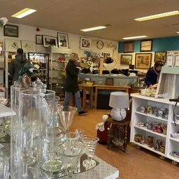 Winkelvloer van kringloopwinkel met glazen serviesgoed op de voorgrond, stellingen met spullen, afdelingen op de achtergrond 