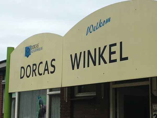 Gevel van kringloopwinkel Dorcas Winkel met crèmekleurige puien en groene zijkant