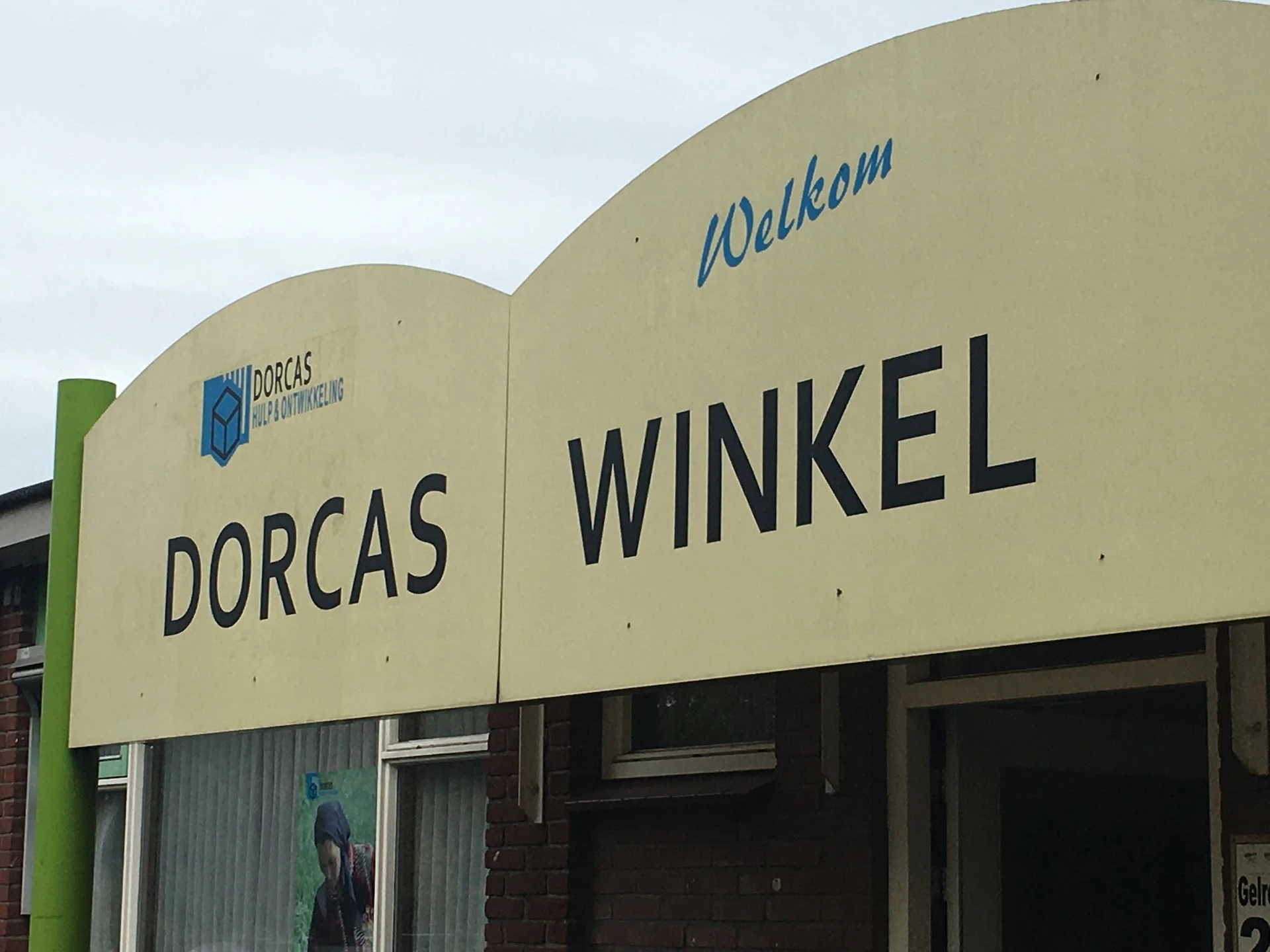 Gevel van kringloopwinkel Dorcas Winkel met crèmekleurige puien en groene zijkant