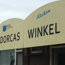 Gevel van kringloopwinkel Dorcas Winkel met crèmekleurige puien en groene zijkant