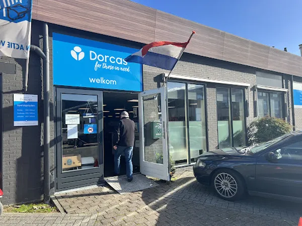 Voorkant van kringloopwinkel Dorcas met blauwe gevel, welkombord en ingang met glazen deuren