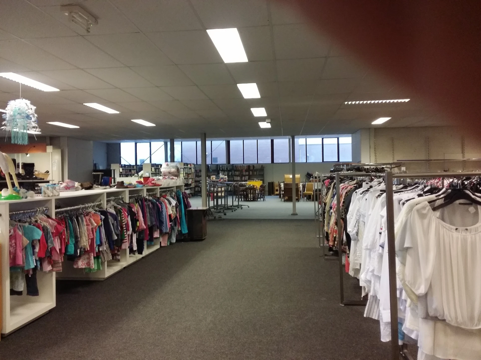 Ruime winkelruimte met kledingrekken vol tweedehands kleding, grote ramen en heldere verlichting