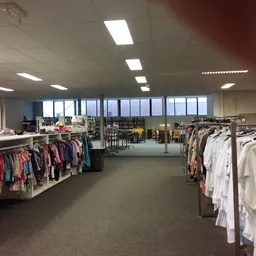 Ruime winkelruimte met kledingrekken vol tweedehands kleding, grote ramen en heldere verlichting