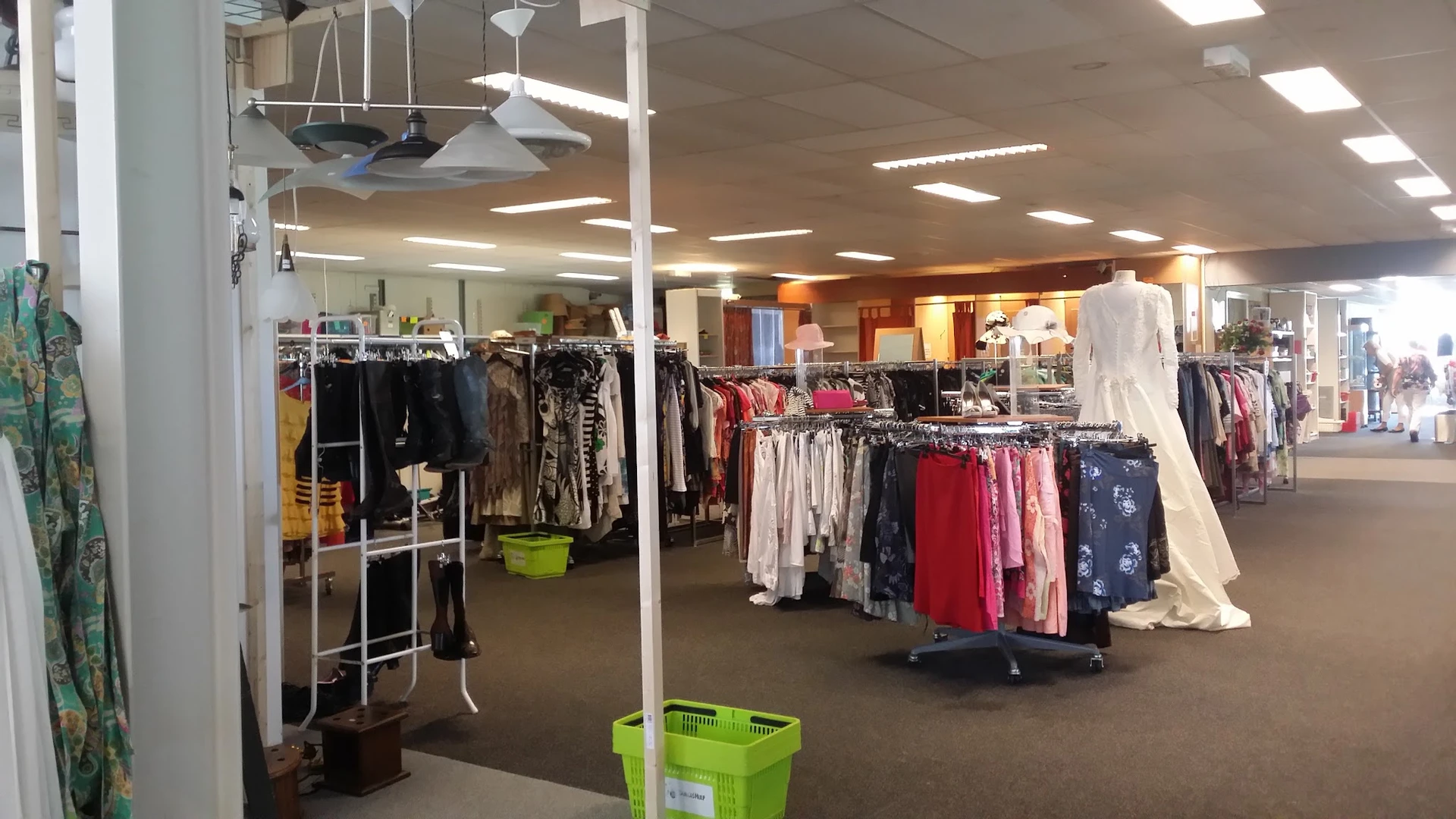 Winkelinterieur met rekken vol tweedehands kleding, groene plastic kratten en hangende kledingstukken