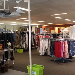 Winkelinterieur met rekken vol tweedehands kleding, groene plastic kratten en hangende kledingstukken