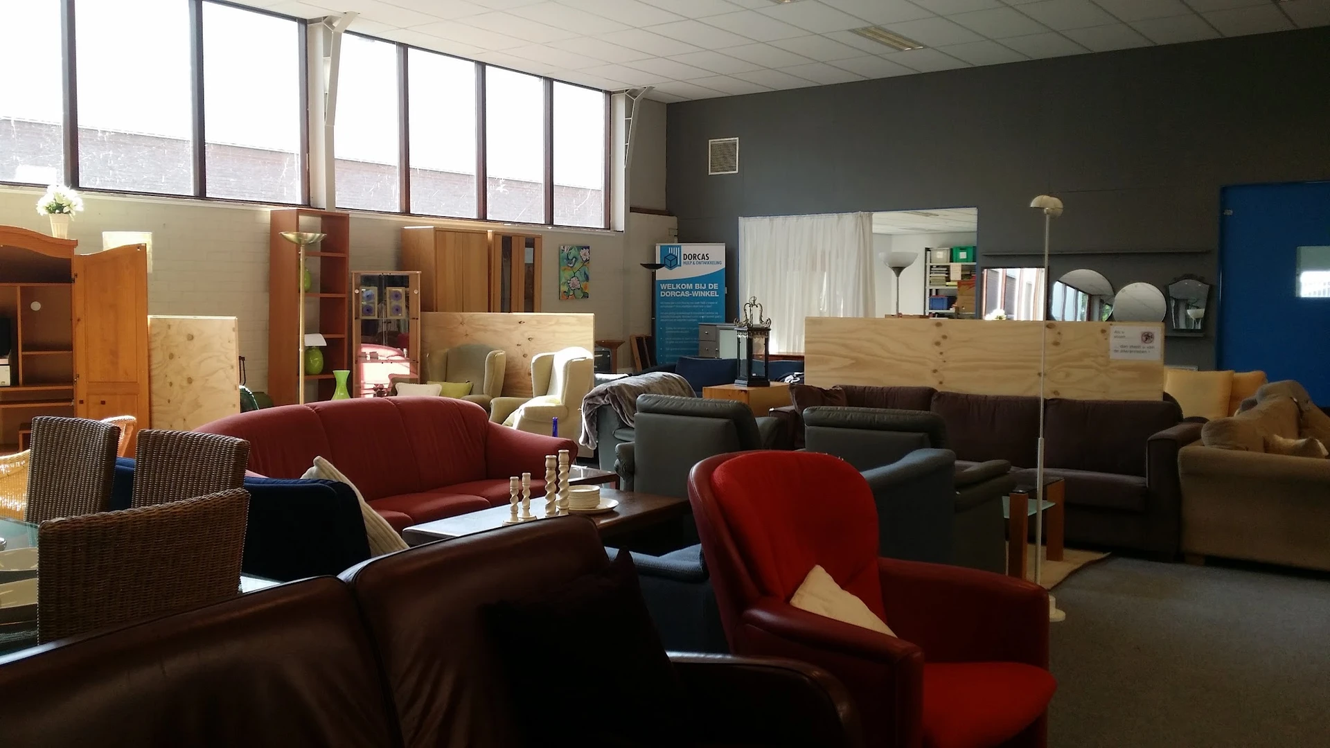 Winkelvloer met diverse meubels: rode en zwarte fauteuils, zwarte kasten, houten kastjes en een donkere muur op de achtergron