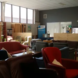 Winkelvloer met diverse meubels: rode en zwarte fauteuils, zwarte kasten, houten kastjes en een donkere muur op de achtergron