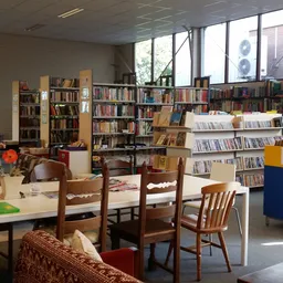 Leeshoek met houten stoelen rond een tafel, boekenkasten en media-uitstalling in kringloopwinkel