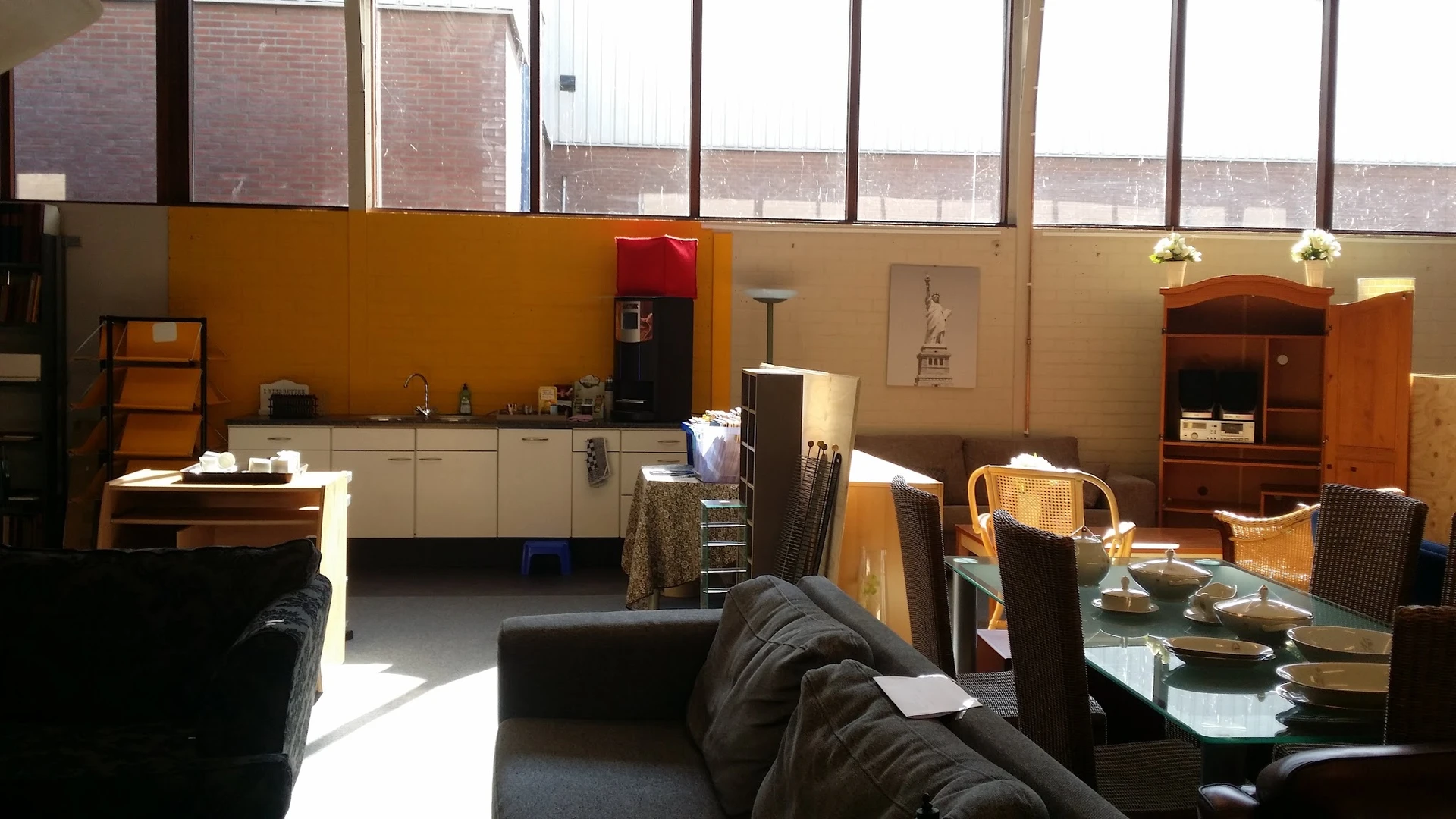 Interieur van kringloopwinkel met zwarte bank, keukenblok, houten stoelen, stellingen en diverse tweedehands meubels