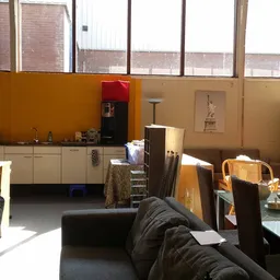 Interieur van kringloopwinkel met zwarte bank, keukenblok, houten stoelen, stellingen en diverse tweedehands meubels