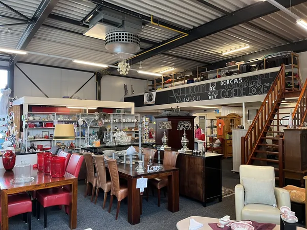 Ruime winkelvloer met donkerhouten eettafel, stoelen, rode accessoires, glazen vitrine, stellingen met spullen en houten trap