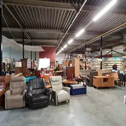Ruim winkelinterieur met diverse meubels, boeken en kringloopwaar, sterke verlichting, betonnen vloer