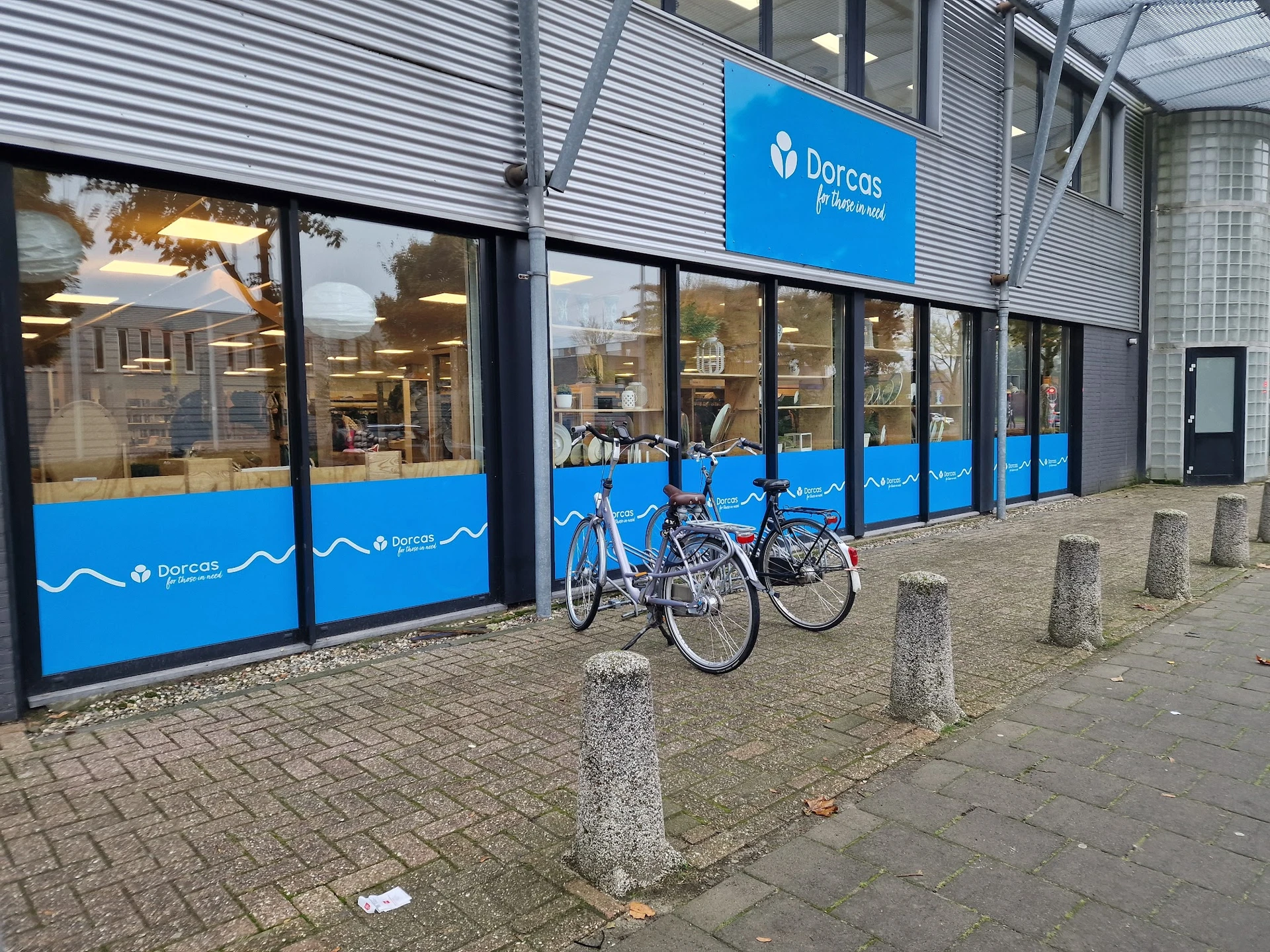 Blauwe gevel van Dorcas kringloopwinkel met grote ramen, twee fietsen geparkeerd ervoor