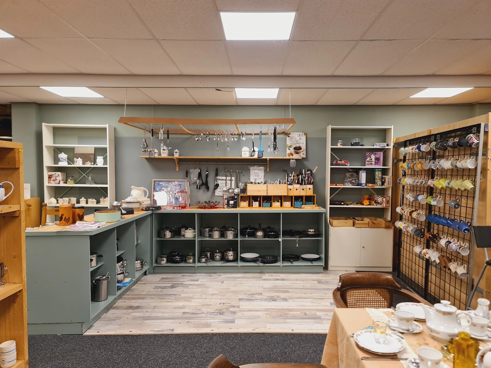 Winkelinterieur met grijze kasten, houten planken, huishoudelijke artikelen en serviesgoed uitgestald