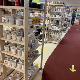 Houten stellingen met diverse witte en grijze mokken, bekers en huishoudartikelen in een kringloopwinkel
