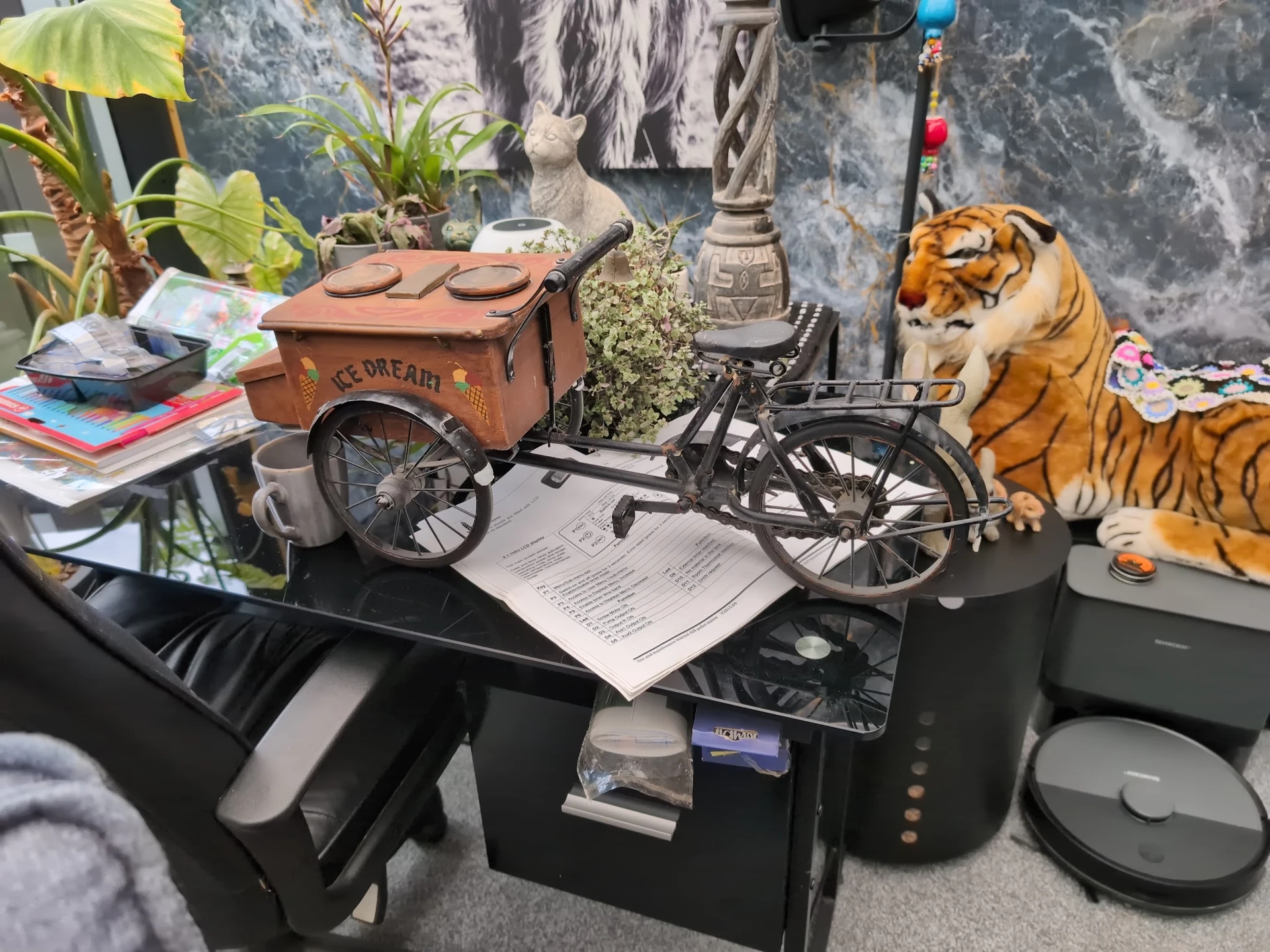 Diverse tweedehands artikelen op een tafel: vintage fietskar, tijger-pluche speelgoed, planten, boeken en huishoudspullen.