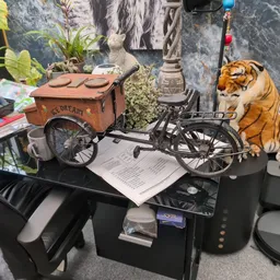 Diverse tweedehands artikelen op een tafel: vintage fietskar, tijger-pluche speelgoed, planten, boeken en huishoudspullen.
