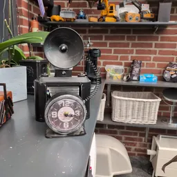 Vintage zwarte telefoon met draaistelsel en klok in voorkant, klokradio op grijze tafel