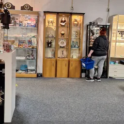 Winkelbinnenruimte met glazen vitrines vol collectibles, beeldjes en decoratieve items. Klant met blauwe winkelmandje kijkt n