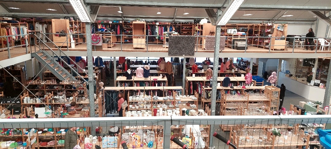 Overzicht van de winkelvloer met verschillende afdelingen, rekken met kleding, boeken en huishoudartikelen op meerdere niveau