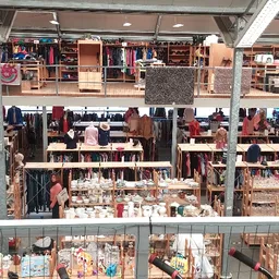 Overzicht van de winkelvloer met verschillende afdelingen, rekken met kleding, boeken en huishoudartikelen op meerdere niveau