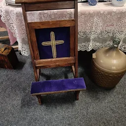 Houten kneelbank met paars fluwelen zitting en goudkleurig kruis op donkerblauw achtergrond