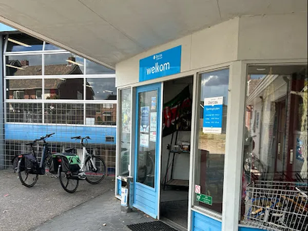 Voorgevel van kringloopwinkel met blauwe accenten, glazen deur en ramen, fietsen buiten geparkeerd