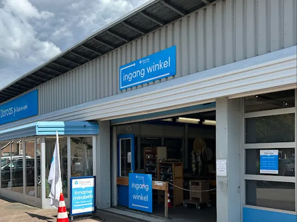 Gevel van kringloopwinkel met blauwe borden 'ingang winkel', glazen deuren en raam aan Nijverheidsweg