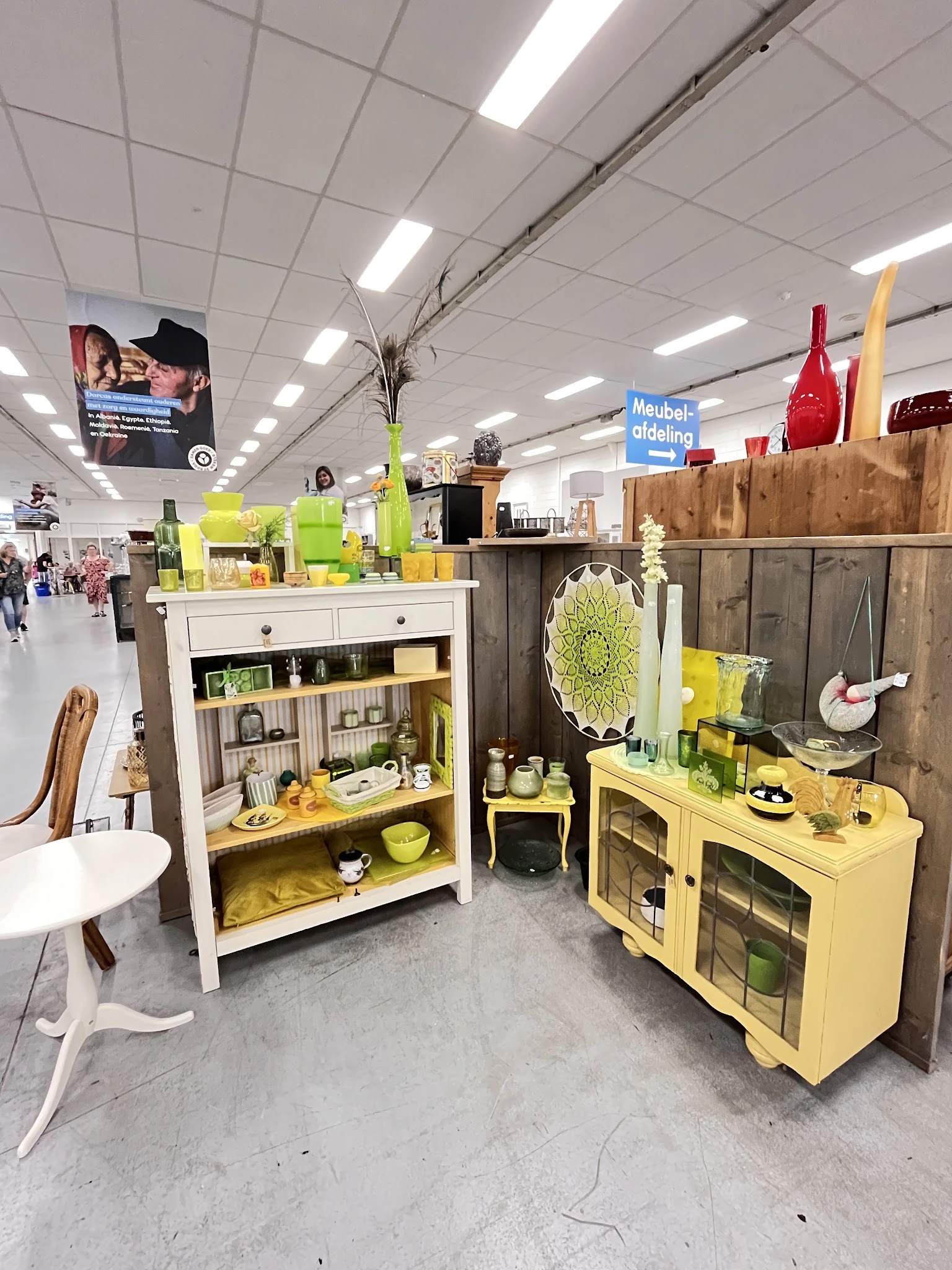 Huishoudelijke artikelen en decoratie in een kringloopwinkel, met geel en groen geschilderde kasten en displays vol servies e