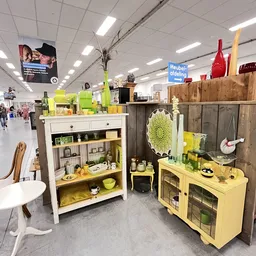 Huishoudelijke artikelen en decoratie in een kringloopwinkel, met geel en groen geschilderde kasten en displays vol servies e