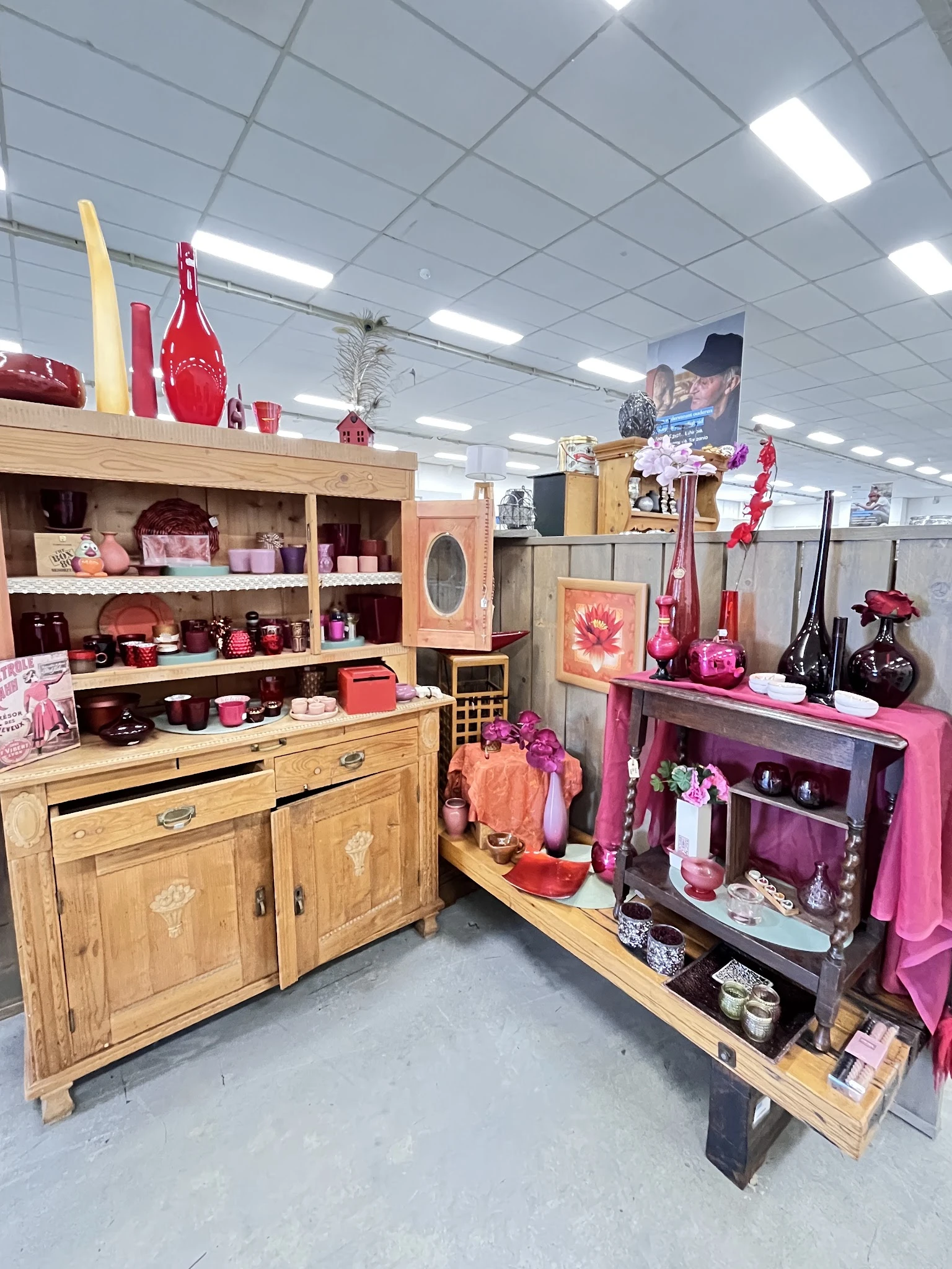 Uitgestalde huishoudartikelen en decoratie in roze en rood tinten op houten meubels en stellingen