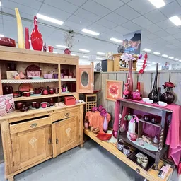 Uitgestalde huishoudartikelen en decoratie in roze en rood tinten op houten meubels en stellingen