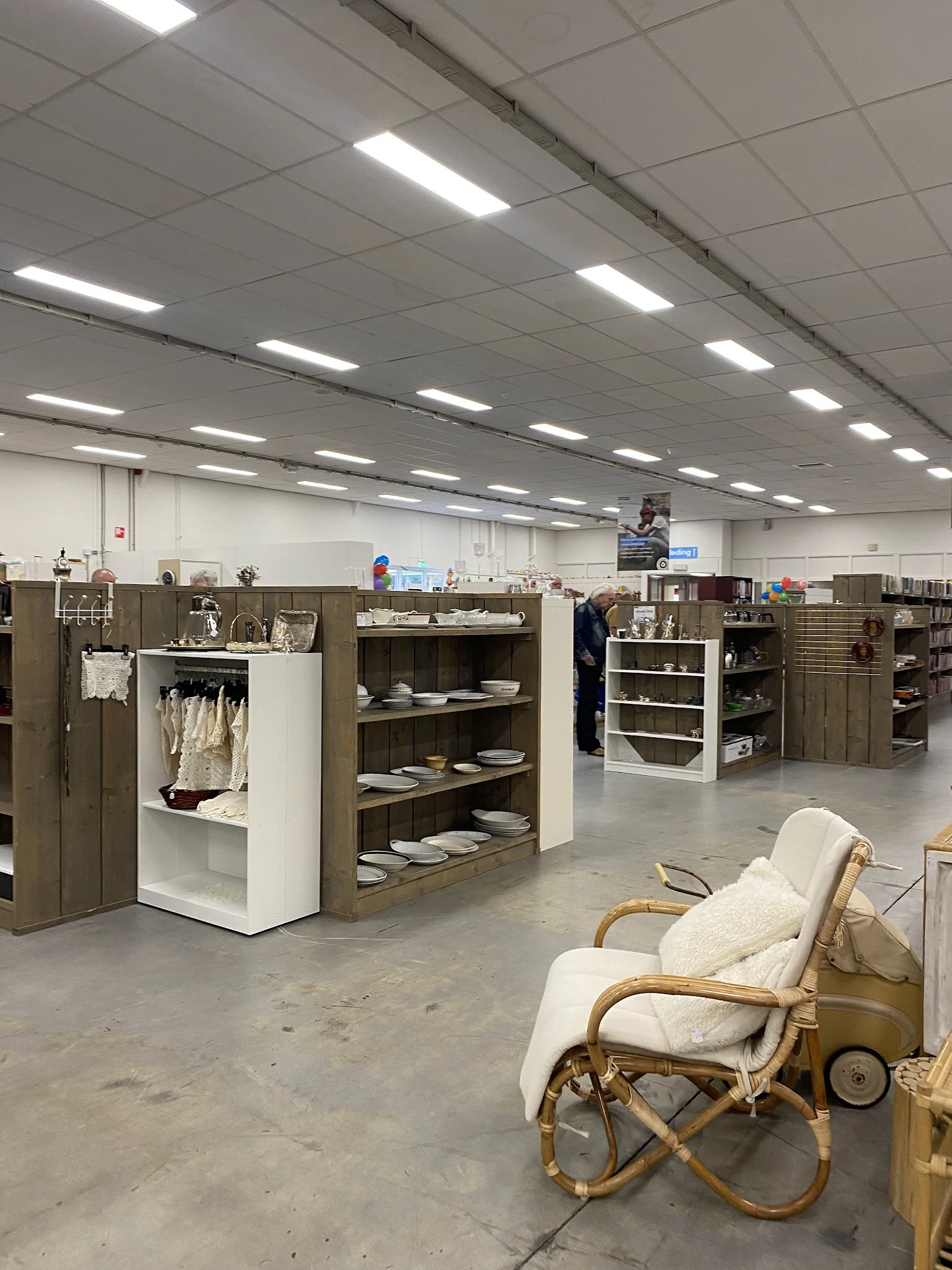 Winkelvloer met stellingen vol servies, borden en huishoudspullen, enkele bezoekers in de kringloopwinkel