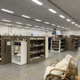 Winkelvloer met stellingen vol servies, borden en huishoudspullen, enkele bezoekers in de kringloopwinkel