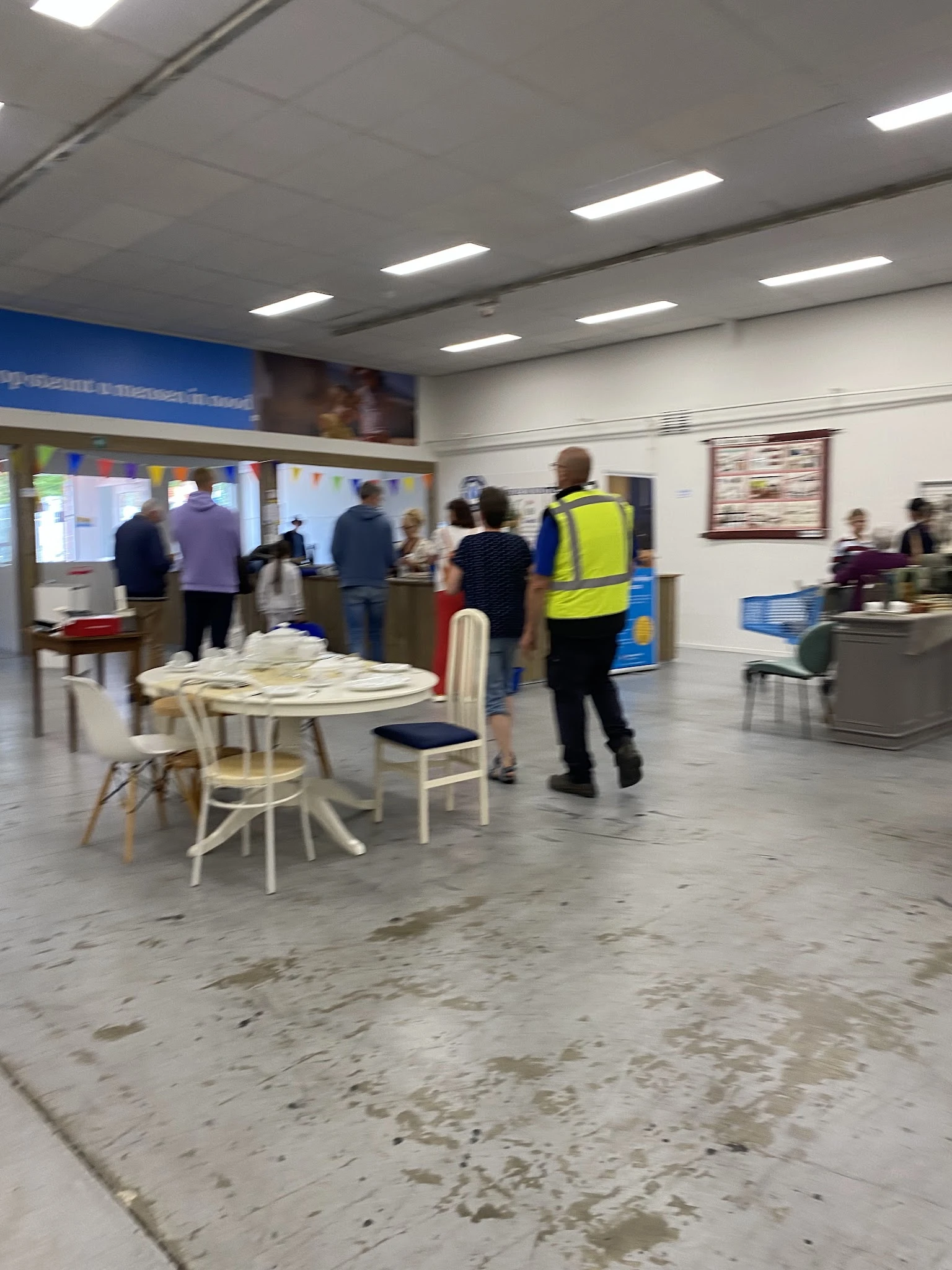 Winkelvloer met ronde tafel en stoelen, bezoekers en personeel in geel hesje in beweging