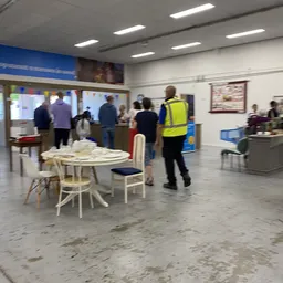 Winkelvloer met ronde tafel en stoelen, bezoekers en personeel in geel hesje in beweging
