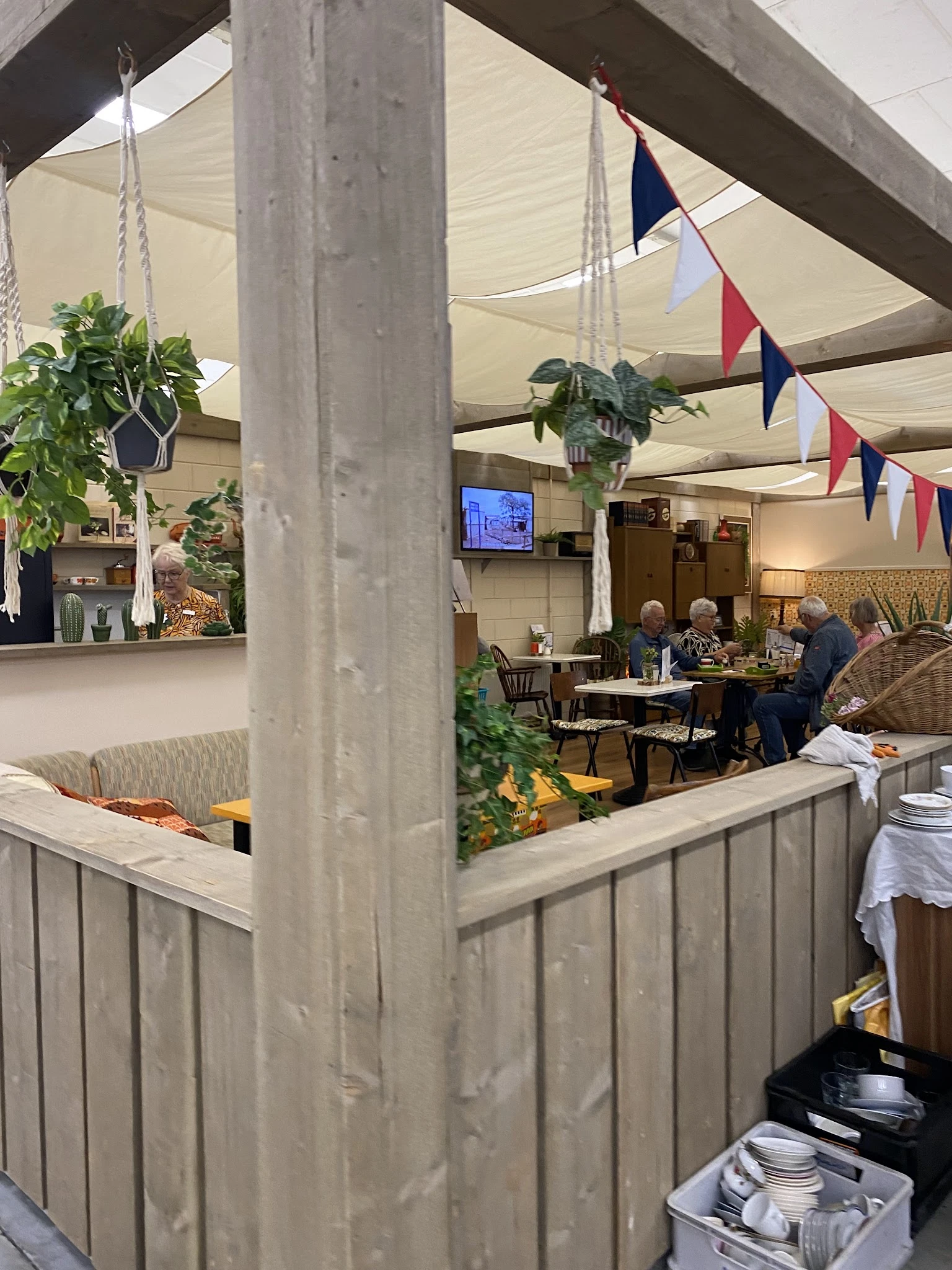 Lunchroom of koffiehoek in kringloopwinkel met bezoekers aan tafels, groene planten en decoratie