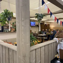 Lunchroom of koffiehoek in kringloopwinkel met bezoekers aan tafels, groene planten en decoratie
