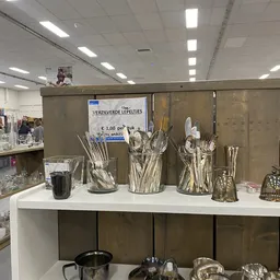 Uitstallingsrek met zilveren bestek in glazen bekers, op witte tafel in kringloopwinkel