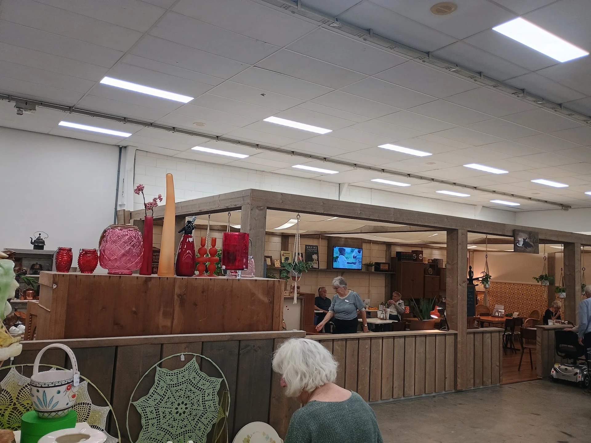 Binnenaanzicht van kringloopwinkel met balie, rode decoratieve items en bezoekers in de winkelruimte
