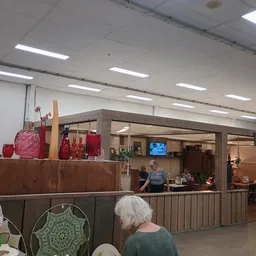 Binnenaanzicht van kringloopwinkel met balie, rode decoratieve items en bezoekers in de winkelruimte