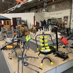 Tweedehands sportapparatuur en fitnesstoestellen uitgestald in de winkel, waaronder hometrainers, halters en andere trainings