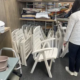 Stapel witte kunststof stoelen in een kringloopwinkel, opgevouwen voor opslag