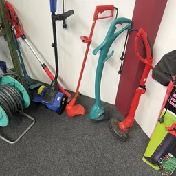 Elektrische tuingereedschap zoals elektrische onkruidverwijderaars en grasmaaiers tegen een muur.